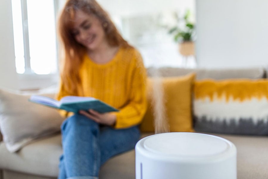 modern-air-humidifier-and-blurred-woman-resting-reading-book-on-sofa-on-background-How-Much-Humidity-Should-be-in-Your-Home